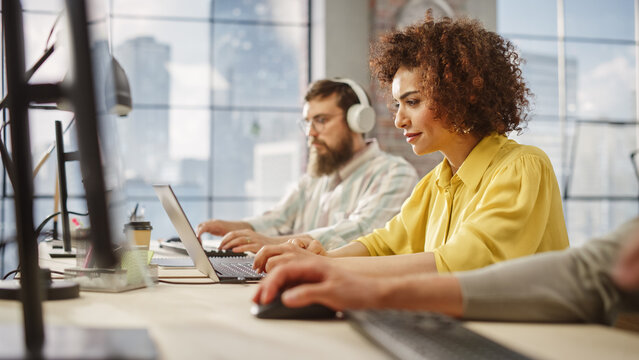Portrait of Creative Biracial Woman Focused on Work While Using a Laptop in a Busy Office. Female Graphic Designer Studying Design Briefs and Making Notes. - Powered by Adobe
