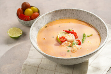 a spicy thai coconut soup or curry made of coconut milk, cherry tomatoes, snow pea, chili pepper, lime, ginger, shrimps and fresh cilantro on kitchen towel on grey concrete background