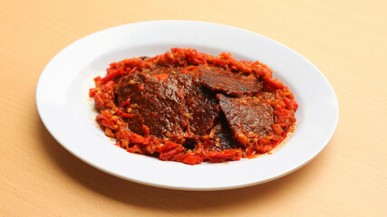 Dendeng balado or jerky beef with spicy seasoning is a traditional cuisine from west sumatera, indonesia. it is made from slice of beef with spicy sauce called sambal. served on plate.