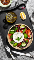 Fototapeta na wymiar Greek salad in a restaurant serving on a black board with olive oil. The salad contains cucumbers, tomatoes, lime, cheese, onions, herbs, spices and lemon. Olive oil salad dressing.