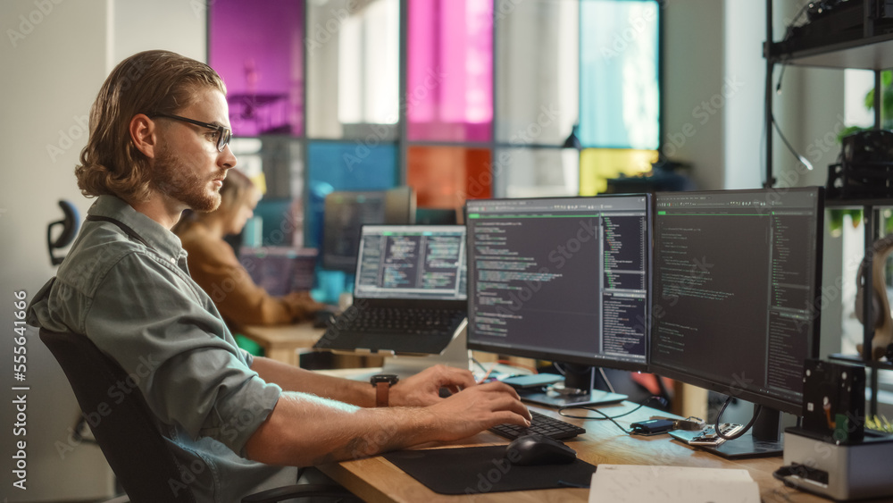Poster Young Caucasian Man Coding on Personal Computer and Laptop Set Up In Stylish Office. Professional Programmer Developing Innovative AI Software in Technological Start-Up, Using Multiple Displays.