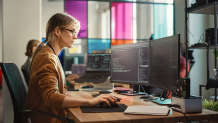 Caucasian Woman Coding on Desktop PC and Laptop Setup With Multiple Displays in Spacious Office. Female Junior Software Engineer Working on New Sprint of Mobile Application Development For Start-up. - obrazy, fototapety, plakaty