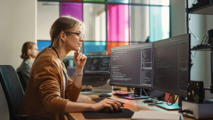 Female Software Engineer Writing Code on Desktop Computer with Multiple Screens Setup in Coworking Office Space. Professional Caucasian Woman Working on SaaS Platform For Innovative Startup.