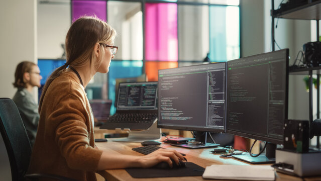 Female Software Engineer Writing Code on Desktop Computer with Multiple Screens Setup in Stylish Coworking Office Space. Professional Caucasian Woman Working on SaaS Platform For Innovative Startup.