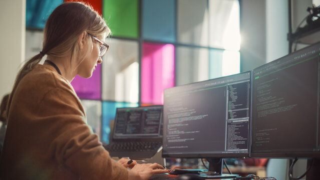 Female Software Engineer Writing Lines of Code on Professional Multiple Display PC Setup In Stylish Office. Caucasian Woman Fixing Bugs and Creating New Features For Innovative Digital Service.