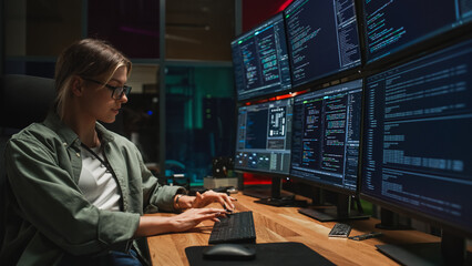 Female Programmer Coding on Desktop Computer With Six Monitors Setup in Dark Office. Smart...