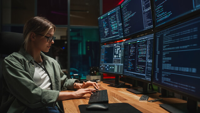 Female Programmer Coding on Desktop Computer With Six Monitors Setup in Dark Office. Smart Caucasian Woman Monitors Data Protection System For Cyber Security Department IT Company
