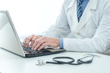 DOCTOR WITH STETHOSCOPE WEARING WHITE LAB COAT USING LAPTOP ON THE DESK IN THE HOSPITAL OFFICE. HEALTH INSURANCE CONCEPT.