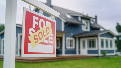 Close Up of a House Sold Sign on a Lawn in Front of a Big Modern House with Traditional...
