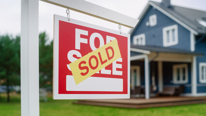Close Up of a House Sold Sign on a Lawn in Front of a Big Modern House with Traditional Architecture. Housing Market Concept with Residential Property in the Countryside.