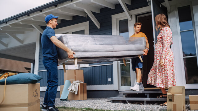 Young Man Helping a Delivery Service Worker to Bring a Modern Couch Into Their New House. Pregnant Female Opens the Door to Let Them Through. Young Family Moving to Their New Home.