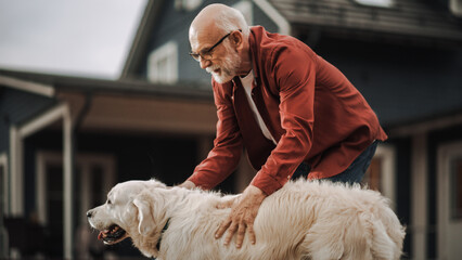 Portrait of a Happy Adult Man Enjoying Time Outdoors with a Pet Golden Retriever, Petting a Playful Dog. Cheerful Senior Male Enjoying Leisure Time in a Garden Lawn in Front of the House.