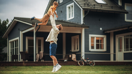 Young Father Playing with His Son Outside the House on the Front Yard. Happy Adult Man Picking Up...