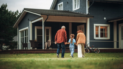 Grandfather and Grandmother Walking Together with Their Granddaughter in Front of their Suburbs...
