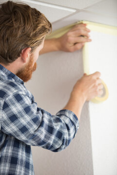 painter applying masking tape to edge of wall