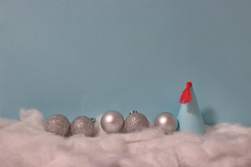round silver ornaments in a row, blue party hat with pink fringe on snow in front of blue background