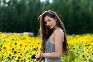 Naklejka na ściany i meble young woman with long hair in linean country style dress walks through a field of sunflowers