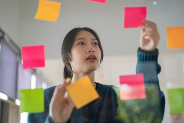 Confident businesswoman planning while looking at adhesive notes stuck on a glass wall.