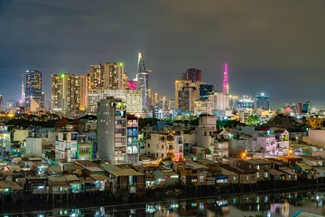Fotobehang HO CHI MINH, VIETNAM - December 3, 2022: Slum wooden house on the Saigon river bank, in front of modern buildings at night in ho chi minh city. View to district 1, see Bitexco tower, Landmark 81. © Quang Ho