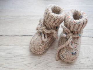 Beige knitted socks, handmade knitted children's shoes from natural wool on a wooden background. Warmth and comfort for newborns. Knitting, needlework, hobby.
