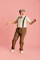 Portrait of emotive senior, old man in stylish classical clothes posing, dancing over pink background. Energy