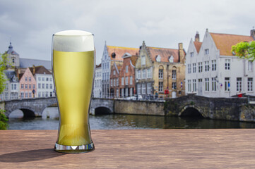 Glass of light beer on wooden table with view of canal and street in Bruges, Belgium