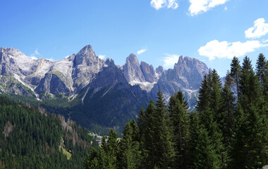 Panorama of Italian Dolomites. Grey huge rocks with green trees around and blue sky. Beautiful nature background.