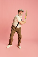 Portrait of emotive senior, old man in classical clothes posing with vintage racket over pink...