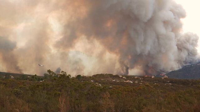 An Airtanker flying through bellowing smoke dropping a fire retardant red chemical Phos-Chek onto a fire in an attempt to contain the blaze during the Fairview wildfires, Hemet, California