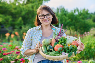 Portrait of smiling woman with basket of different fresh vegetables and herbs