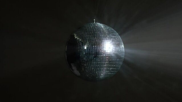Disco Ball with Reflected Moving Rays Rotating. Mirror disco ball in white light. Isolated disco ball on black background. Close-up. Mirror ball spinning indoors. Performance. The reflection of lights