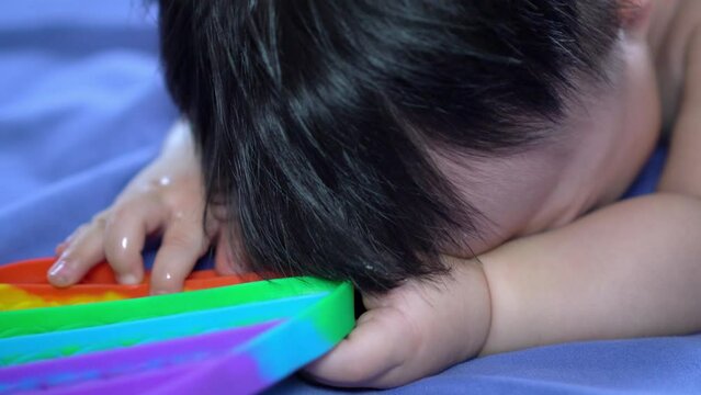 Chinese baby boy hold rainbow color sensory toy cry at bed