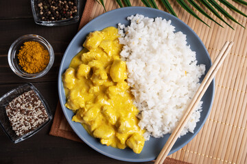 Boiled rice with chicken in curry sauce on a blue plate and bamboo napkin.