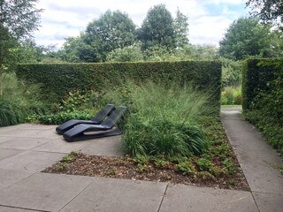 Sun loungers in the garden. Modern patio with two black deck chairs next to the green trimmed bushes in summer garden. The Mien Ruys Gardens, The Netherlands, August 4, 2019