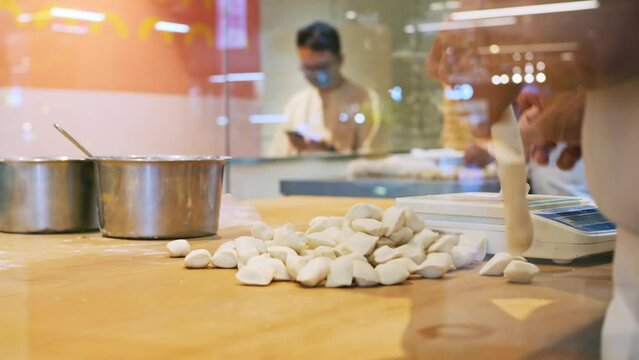 The cook in the open kitchen prepares dough dishes, his work is watched by restaurant visitors. A cook in a restaurant prepares a dumpling from dough and minced meat. Chinese dumplings in a restaurant