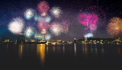 Fototapeta premium Colorful fireworks display over city on the beach. Firework celebration sparkling in midnight sky, sea