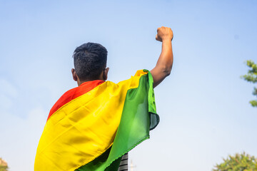 Back view shot of man with black history month flag on shoulder by raising fist hand - concept of...