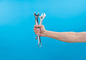 Human hand holding wrenches on blue background