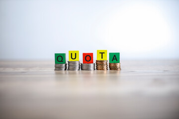 The word QUOTA written on the wooden cubes placed on the stacked coins