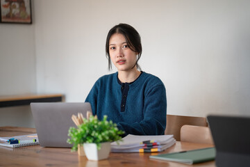 Beautiful Asian woman working on a laptop at work. She looked straight at the camera and showed confidence.