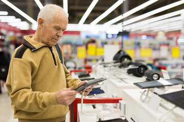 elderly man examines tablet computer in showroom of electronics store