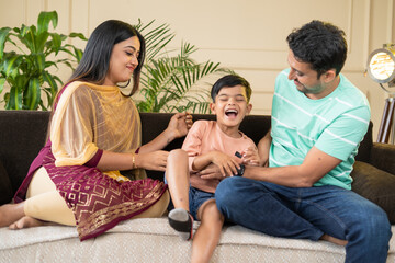 focus on mother, Happy smiling couples playing with kid by tickling or cuddling on sofa at home -...