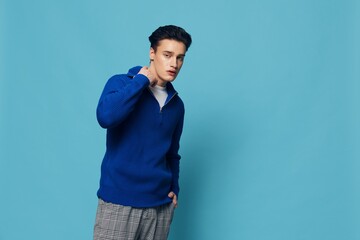 Fototapeta premium photo of a handsome, stylish man in a blue zip-up jacket standing on a light blue background adjusting the collar with his hands