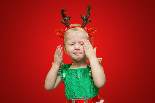A child in a carnival costume celebrates Christmas. A little girl with Klaus deer horns closed her eyes and covered her face with her hands.