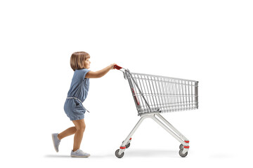 Full length profile shot of a little girl pushing a big empty shopping cart