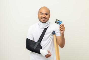 Asian man broken arm and leg holding credit card payment. Man put on plaster cast splint with...