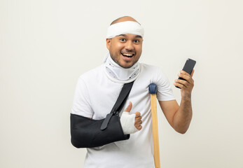 Happy young asian man broken arm holding smartphone. Asian man put on plaster bandage cast splint....