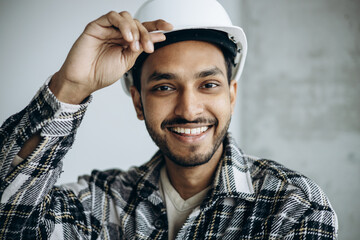Indian workman wearing white hard hat standing isolated on gray background