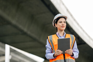 Asian engineer worker woman or architect looking construction with tablet wear white safety helmet...