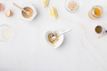 Flatlay with homemade beauty products: fresh ingredients like oat, honey, lemon, banana, egg, olive oil. Female hand holding a jar of cream. Overhead view, copy space.